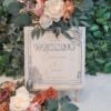 Personalised Botanical Frame Wedding Welcome Sign in square format, layered wooden design with floral corner details, custom names and wedding date, displayed on wooden stand